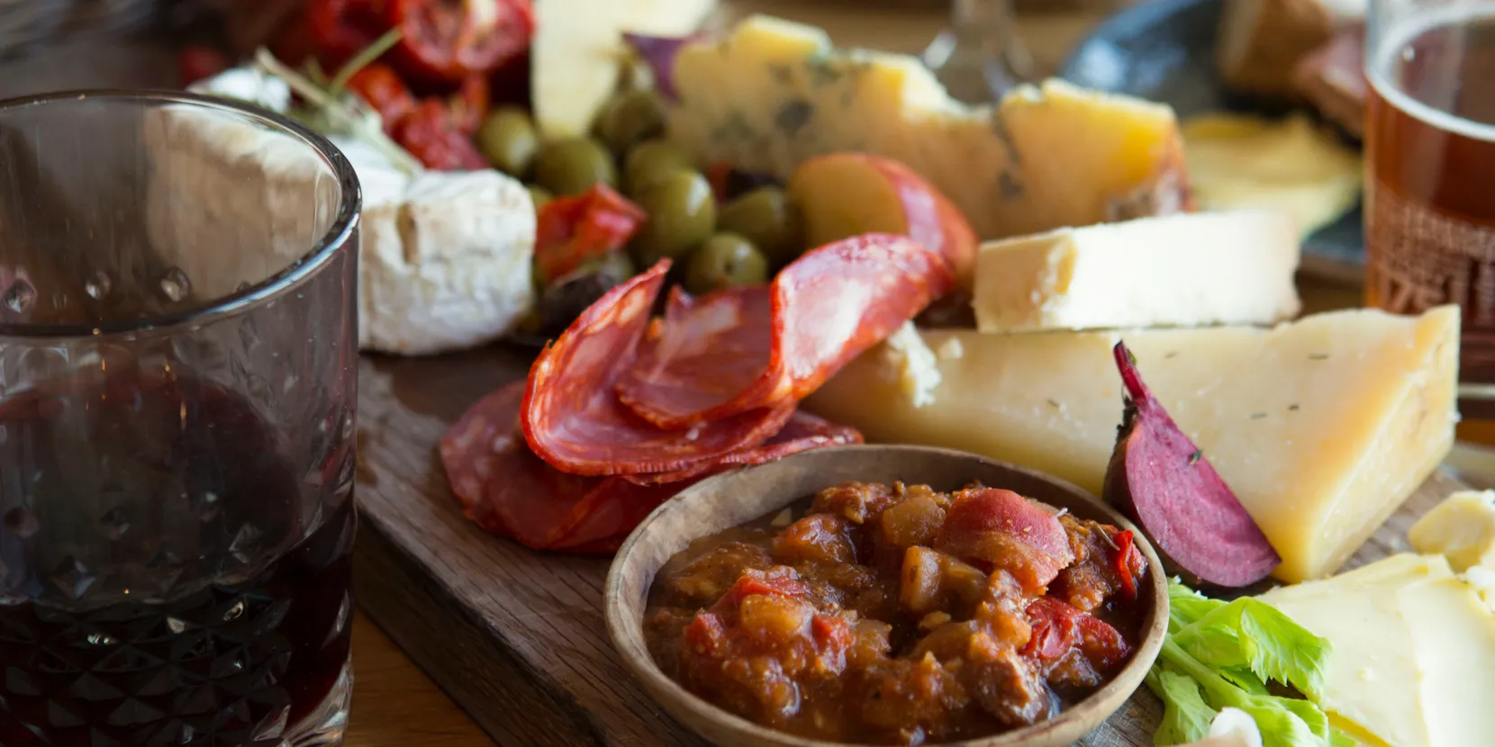 Sharing board with cheeses, chorizo, olives and chutney beside a glass of red wine
