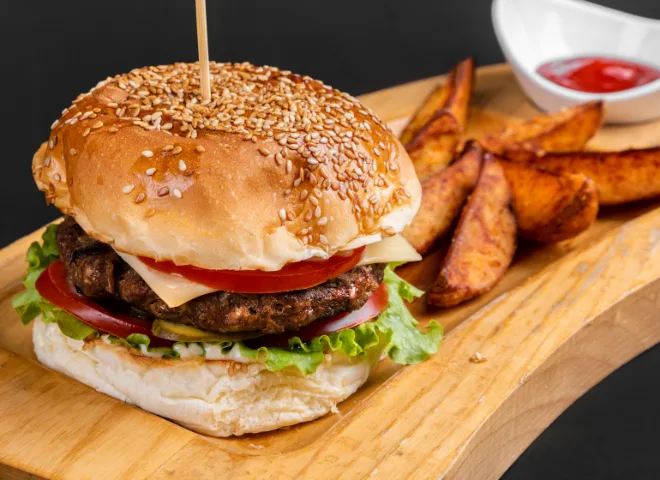 A cheese burger on a wooden platter. Potato wedges next to it