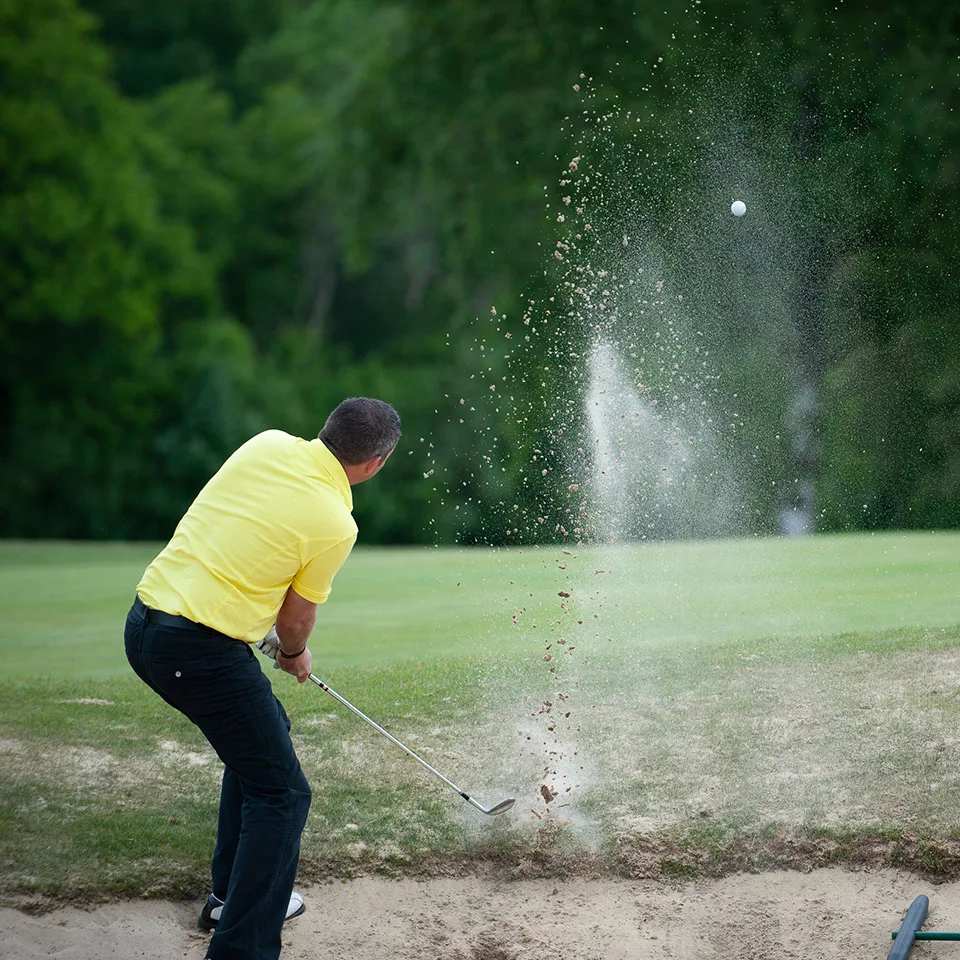 Golfer playing out of a bunker in a spray of sand