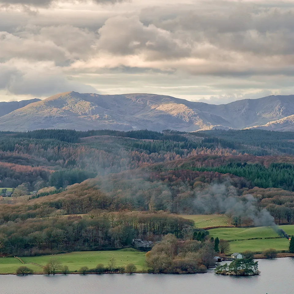 Lake District fells and woodland above a lake on a cloudy day