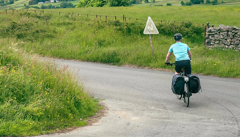 Cyclist with panniers riding a country lane through green countryside