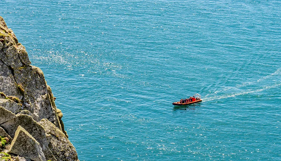 Small boat of passengers on turquoise sea beside a rocky cliff